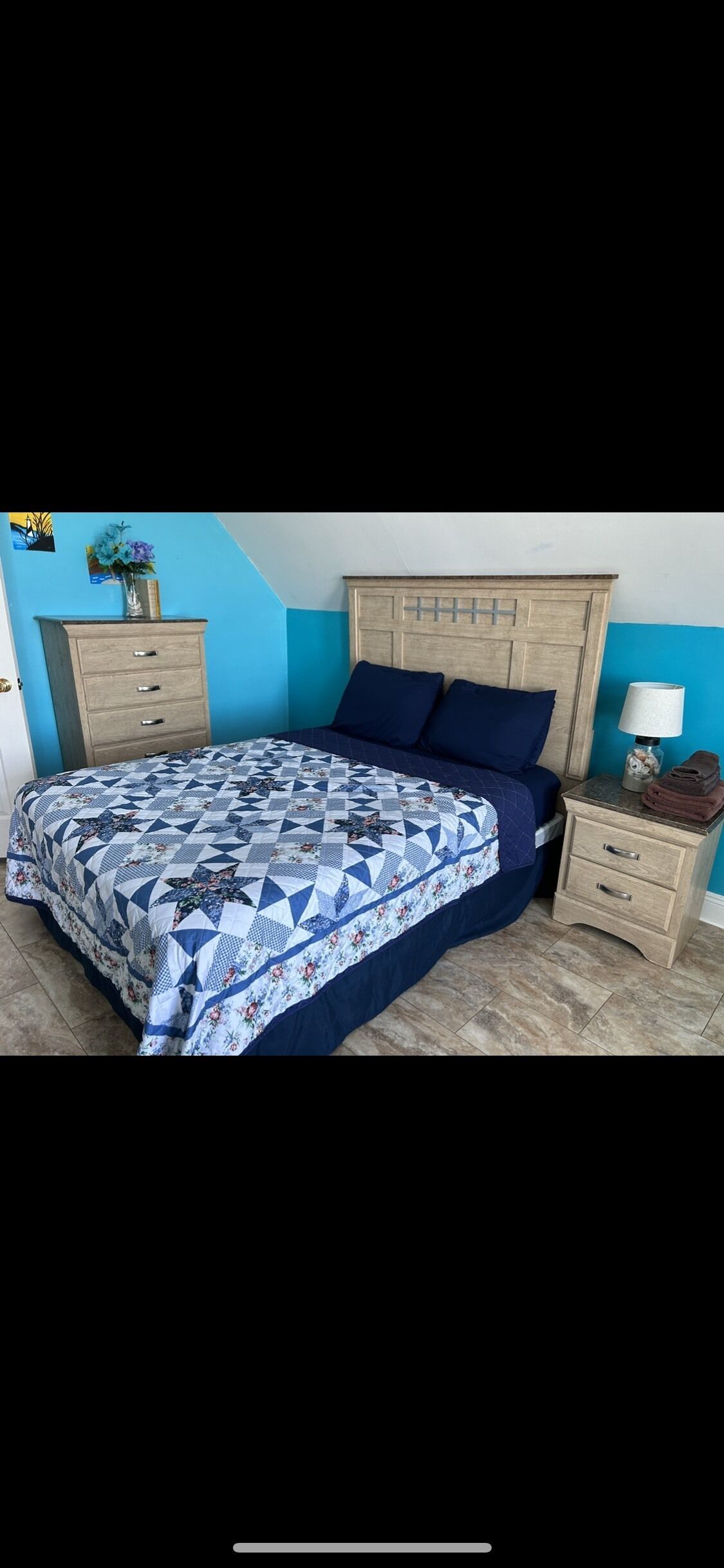 A bedroom with a bed, a nightstand, a dresser, and a wall with a blue and white color scheme.