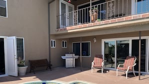 A residential outdoor area with a swimming pool, a barbecue grill, a bench, and two chairs.