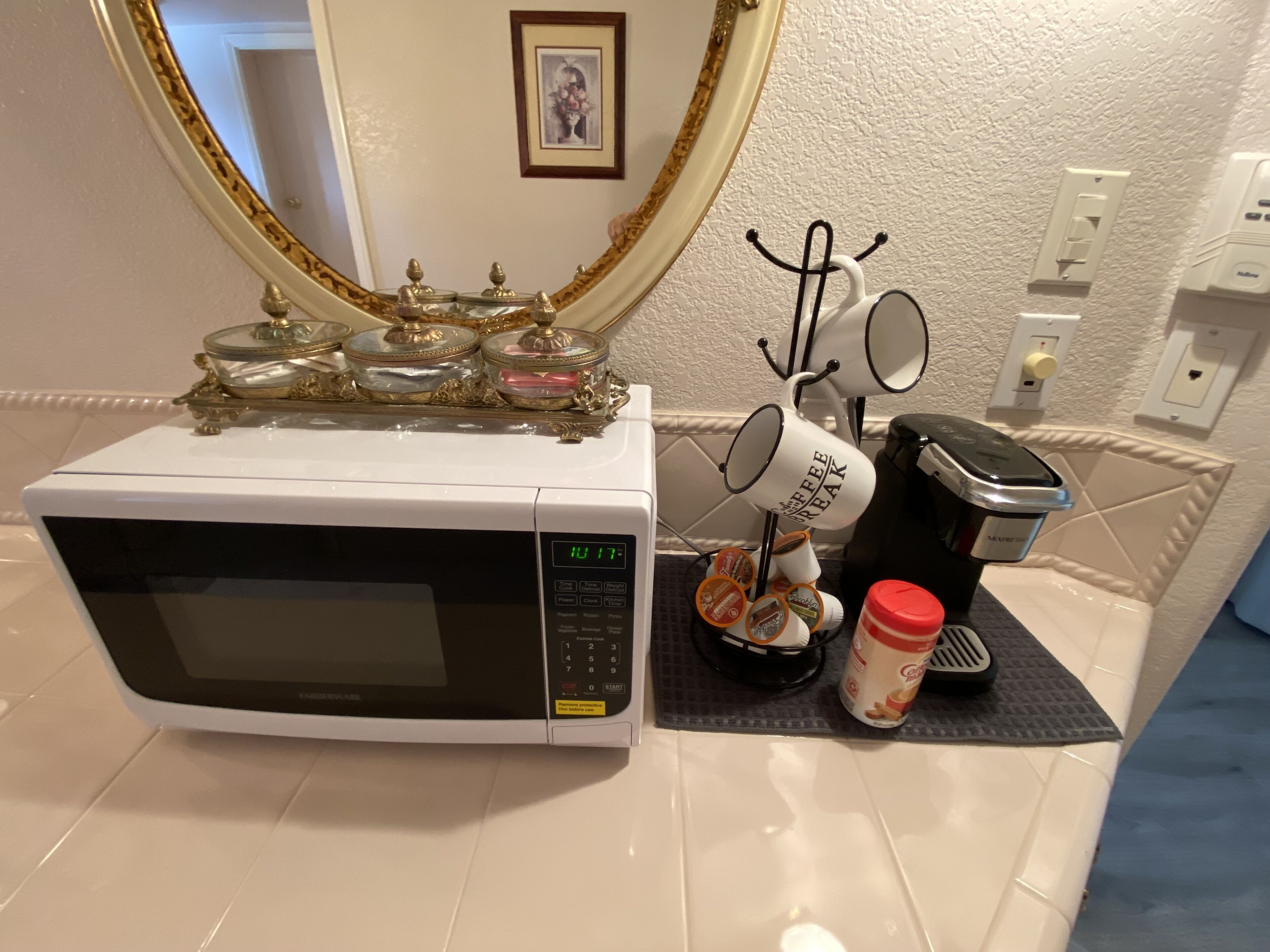 Un horno microondas con pantalla digital, una cafetera y un hervidor de agua sobre una encimera.