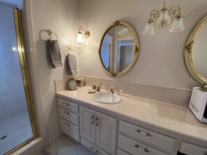 Une salle de bain avec un meuble-lavabo blanc, des miroirs encadrés d’or et un lavabo blanc.
