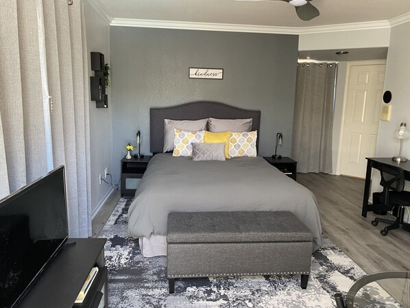Une chambre à coucher comprenant un lit, des tables de chevet, un banc, un téléviseur et un ventilateur de plafond.