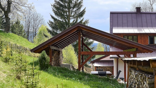 A wooden structure with a sloped roof, surrounded by a lush green hillside and a mountain in the background.