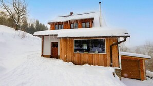 A wooden cabin with a chimney, a garage, and a snow-covered roof.