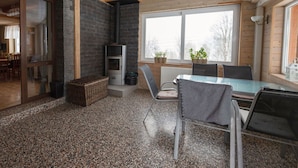 A cozy cabin interior with a stone fireplace, a dining area with a glass table, and a view through large windows.