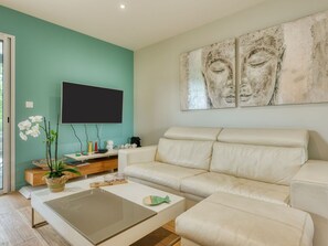 Uma sala de estar com parede azul-turquesa, um sofá branco, uma mesa de centro e uma televisão de tela plana fixada na parede.