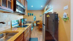 A compact kitchen with a stainless steel sink, a microwave, and a refrigerator. There is a dining area with a table and chairs, and artwork on the walls. - Walk to Sandfest, Shared Pools, Boardwalk to the Beach (Port Aransas)