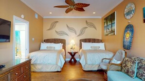 A hotel room with two beds, a ceiling fan, a TV, a wall clock, and a beach-themed wall decoration. - Walk to Sandfest, Shared Pools, Boardwalk to the Beach (Port Aransas)
