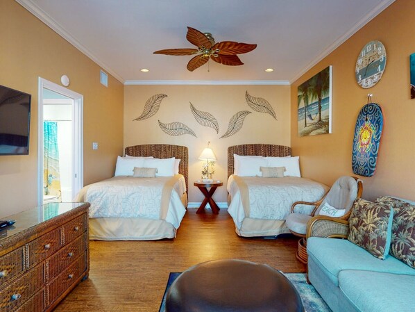 A hotel room with two beds, a ceiling fan, a TV, a wall clock, and a beach-themed wall decoration. - Walk to Sandfest, Shared Pools, Boardwalk to the Beach (Port Aransas)