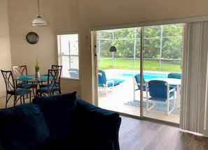 Una habitación con una mesa de comedor, sillas, un sofá, un reloj y una puerta corrediza de vidrio que da a una zona de piscina.