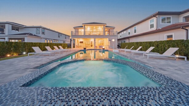 Ein modernes, zweistöckiges Haus mit Swimmingpool, Liegestühlen und einer gut beleuchteten Eingangspartei.