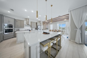 A modern kitchen with a large island, stainless steel appliances, and pendant lighting. - Mania Bear's Den Mansion With Themed Bedrooms at Reunion (Kissimmee)