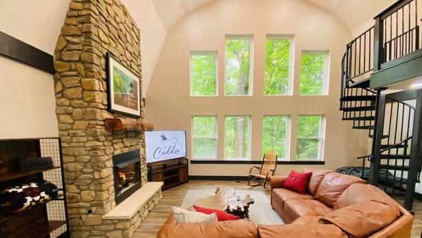 A cozy living room with a stone fireplace, a large sectional sofa, and a TV mounted on the wall. - Fully Renovated Cabin in Hocking Hills - Hot Tub, Game Room, Wifi, Fireplace (Amanda)