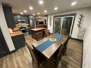 A modern kitchen with dark cabinets, stainless steel appliances, and a wooden dining table with chairs. - Fully Renovated Cabin in Hocking Hills - Hot Tub, Game Room, Wifi, Fireplace (Amanda)