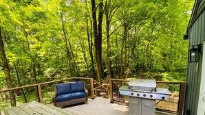 A deck with a grill, a sofa, and a table. - Fully Renovated Cabin in Hocking Hills - Hot Tub, Game Room, Wifi, Fireplace (Amanda)