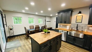 A modern kitchen with a central island, dark cabinets, and a dining area with chairs and a table. - Fully Renovated Cabin in Hocking Hills - Hot Tub, Game Room, Wifi, Fireplace (Amanda)