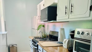 A compact kitchen with white cabinets, a stainless steel stove, a microwave, a toaster, and a sink.