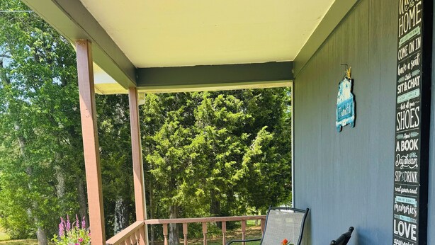 A covered porch with wooden flooring, two chairs, a table, and potted plants.