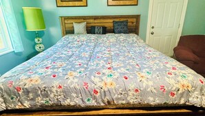 A bedroom with a floral bedspread, a wooden headboard, a green lamp, and a door with emergency exit signs.