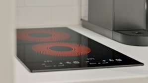 A modern kitchen with a built-in induction cooktop and a stainless steel range hood. - La Dolce Vita Studio (Port St. Lucie)