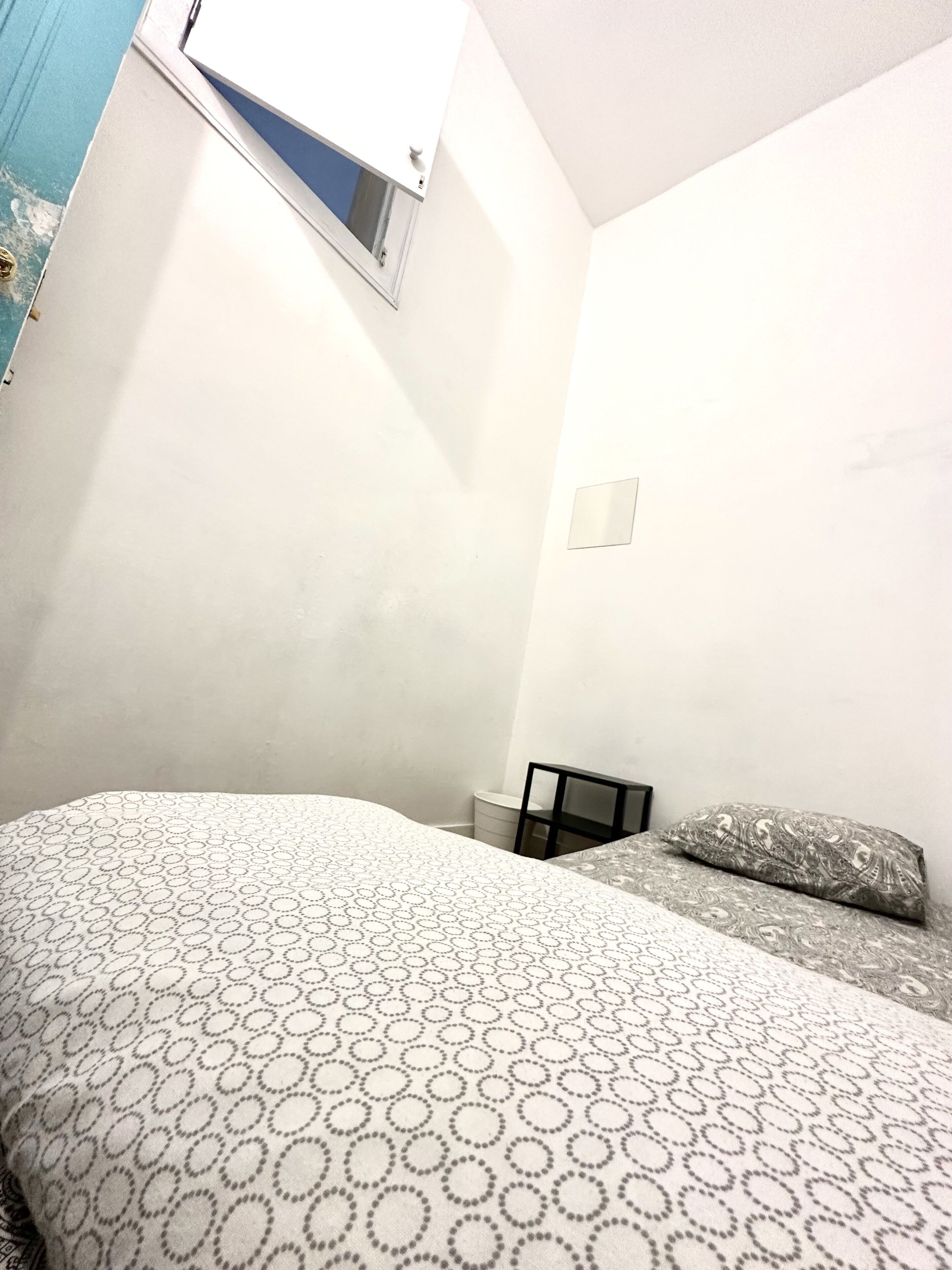 A bedroom with a bed, a small table, and a window.