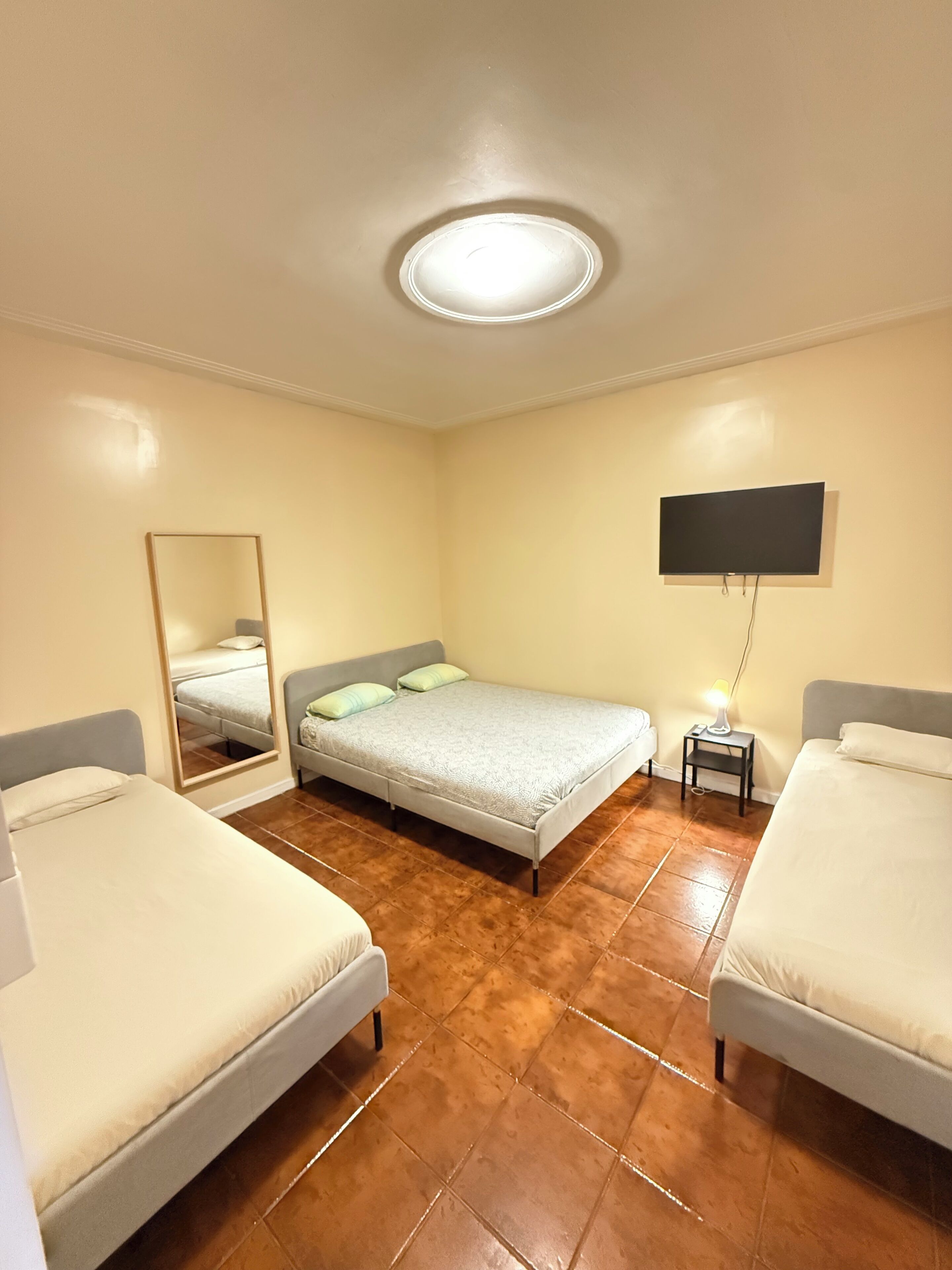 Une chambre avec deux lits, un téléviseur à écran plat, un miroir et une petite table de chevet avec une lampe.