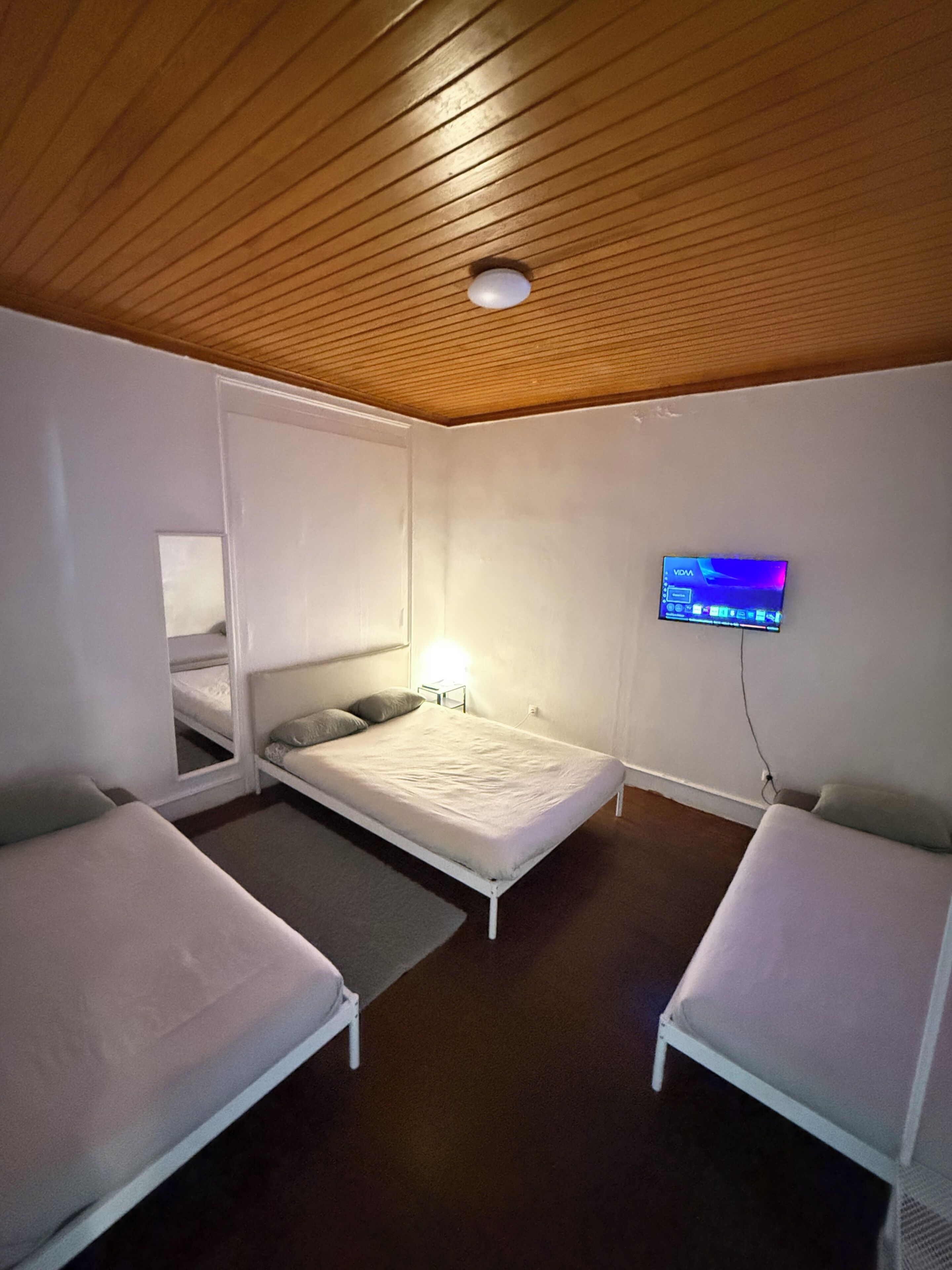 Una camera con due letti singoli, una piccola TV fissata al muro e un soffitto in legno.