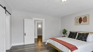 A bedroom with a bed, a door, a plant, and a wall with a painting. - Gatsby vibes house in Old Oaks, close to everything (Columbus)
