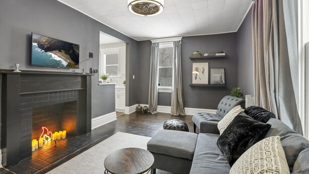 A modern living room with a fireplace, grey walls, a grey sofa, and a large window. - Gatsby vibes house in Old Oaks, close to everything (Columbus)