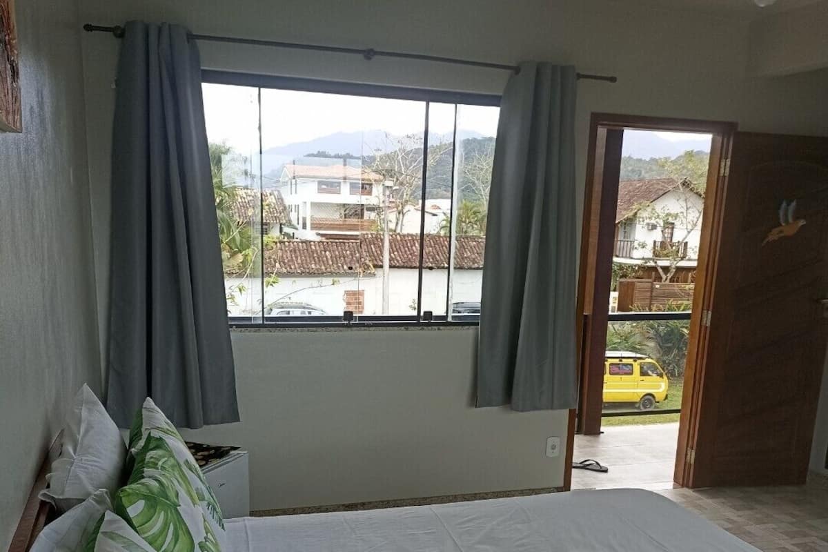 A bedroom with a bed, curtains, a window, and a view of the outside.
