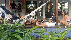 A covered outdoor seating area with a hammock, people relaxing, and a view of a building with a balcony. - Pousada Tropicália Paraty (Paraty)