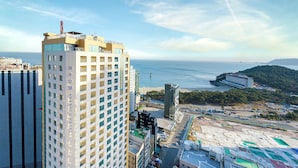 A high-rise hotel with multiple floors, a prominent antenna, and a view of the sea and distant hills. - Kwangsu Hotel (Busan)
