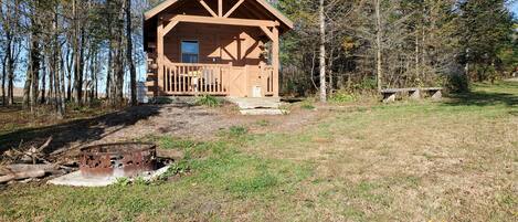 A wooden cabin with a porch, surrounded by trees.