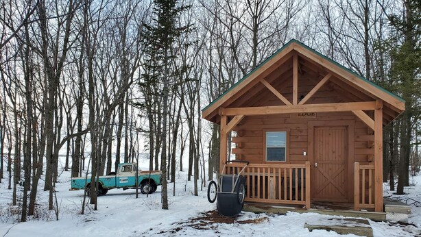 Una baita di legno con un portico, circondata da alberi e terreno innevato.