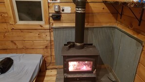 Un accogliente chalet con stufa a legna, un letto piccolo e una finestra.