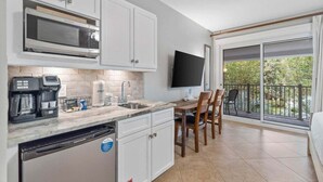A modern kitchen with white cabinets, a built-in microwave, and a coffee maker. There is a dining area with a table and chairs, and a large window with a view of greenery.