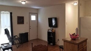 Ein Wohnzimmer mit Flachbildfernseher, Holzschrank, Stuhl und kleinem Tisch.