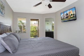 Une chambre à coucher avec un lit, un ventilateur de plafond, un téléviseur fixé au mur et une fenêtre.