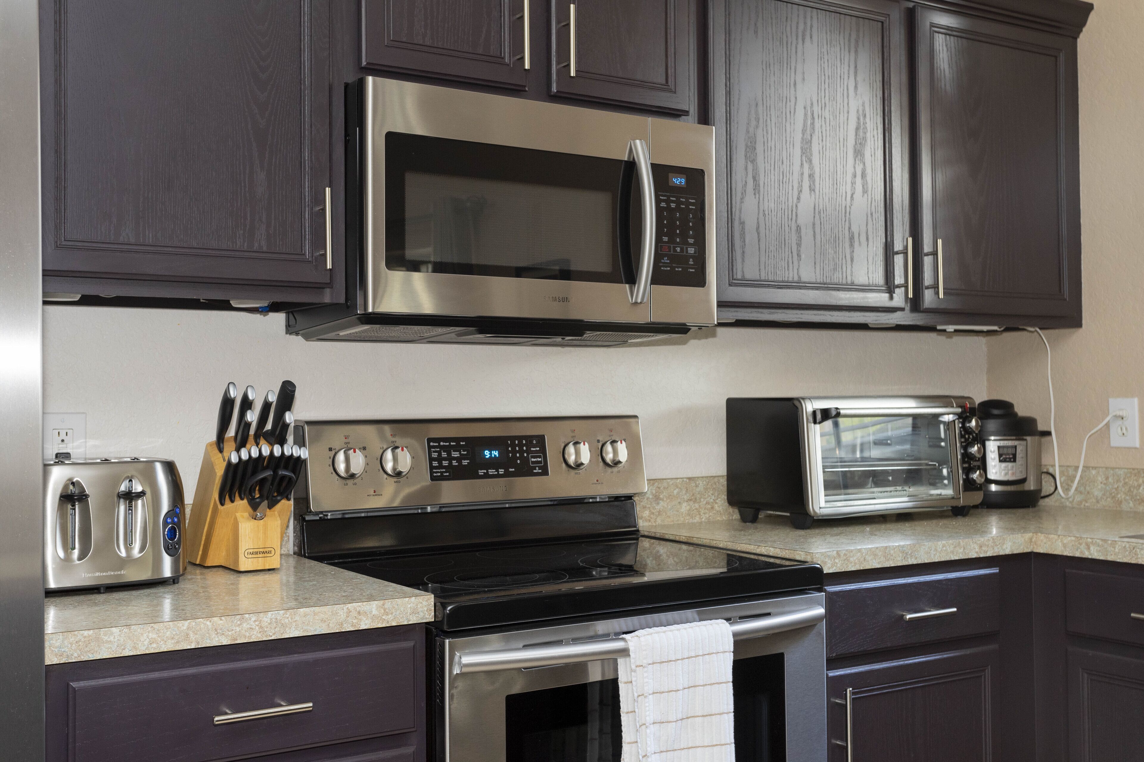 A kitchen with dark wood cabinets, stainless steel appliances including a microwave, toaster, and oven, and a knife block on the counter.