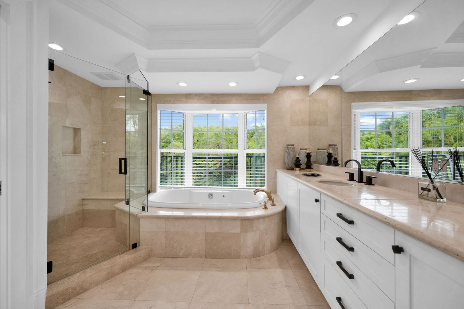 A modern bathroom with a freestanding bathtub, a glass-enclosed shower, and a large window offering a view of greenery.