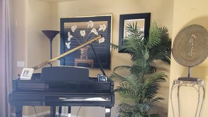 A grand piano in a well-lit room with a large potted plant, framed artwork on the wall, and a small table with a picture frame. - Spanish Villa with heated pool, hot tub and outdoor living space (Phoenix)