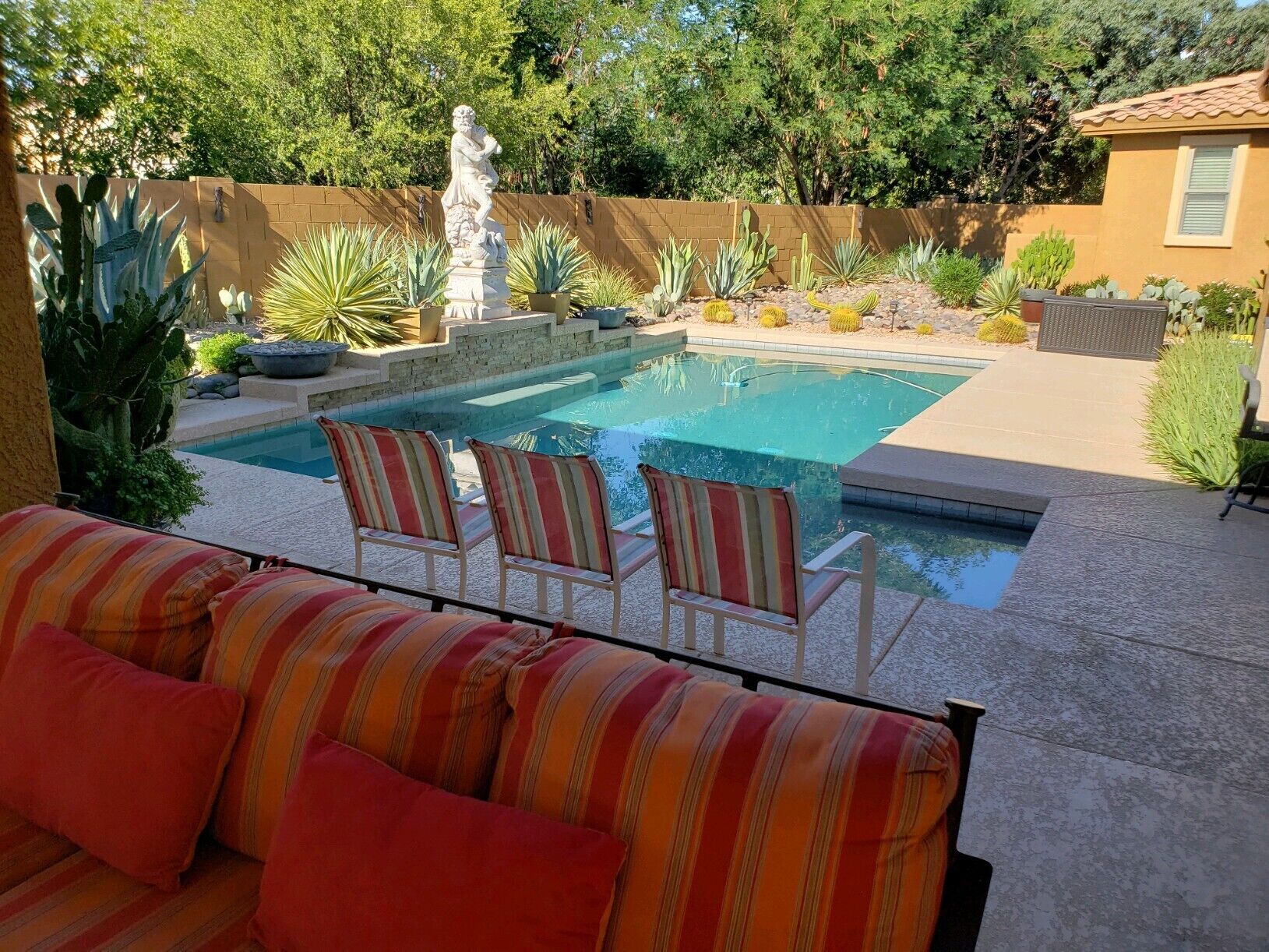 Una piscina con una estatua, rodeada de cactus y sillas.