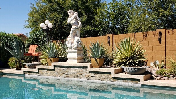 A swimming pool with a stone border, a statue, and various potted plants. - Spanish Villa with heated pool, hot tub and outdoor living space (Phoenix)