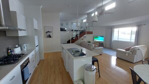 A modern kitchen with a central island, a dining area with a table and chairs, a living room with a sofa, and a TV. - Townhouse close to shelly beach Port Macquarie (Port Macquarie)