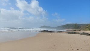 A sandy beach with waves, rocky outcrops, and a distant mountain. - Townhouse close to shelly beach Port Macquarie (Port Macquarie)