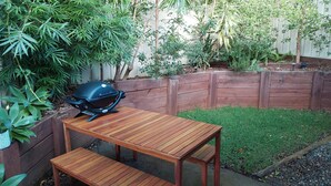 A wooden table and bench set in a backyard with a barbecue grill. - Townhouse close to shelly beach Port Macquarie (Port Macquarie)