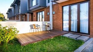 A modern residential building with a wooden deck, outdoor seating, and a well-maintained garden. - De Hsahe Villa (Tabanan)