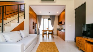 A modern living room with a sofa, TV, wooden staircase, kitchen area, and dining table. - De Hsahe Villa (Tabanan)
