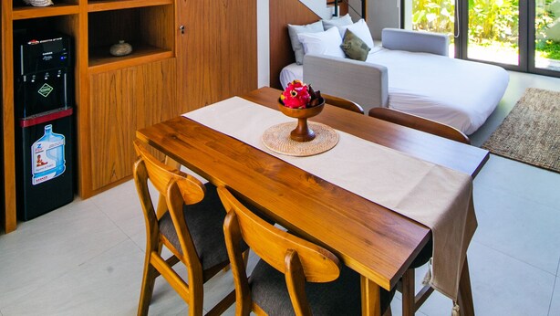 A modern kitchen with wooden cabinetry, a dining table with chairs, a black pendant light, and a staircase leading to a bedroom with a large window. - De Hsahe Villa (Tabanan)