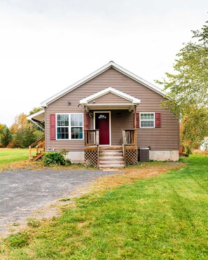 Une maison à deux étages avec une porte d’entrée rouge, un porche et un petit jardin devant.