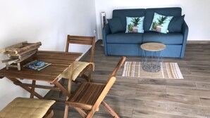 Ein Essbereich mit einem Holztisch und Stühlen, einer blauen Couch mit gemusterten Kissen sowie einem kleinen runden Tisch und einem gewebten Hocker.